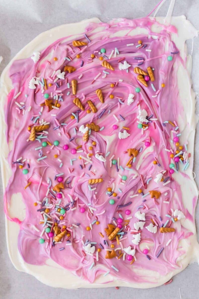 Unicorn bark topped with colorful sprinkles, mini pretzel pieces, and small candy shapes on a flat surface.