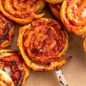 Close-up of bbq tortilla roll ups with visible tomato sauce, cheese, and crispy edges, one being lifted with a metal spatula.