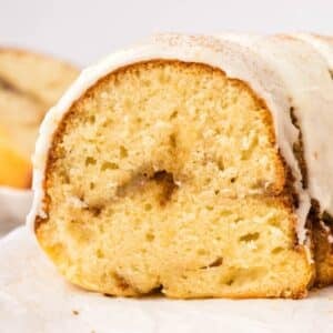 A close-up of a sliced cinnamon bundt cake with white icing and a dusting of cinnamon on top.