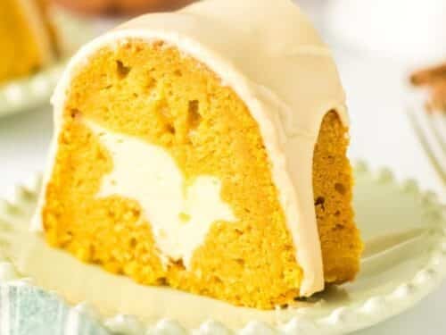 A slice of pumpkin bundt cake with cream cheese filling and light glaze, served on a pale green plate.