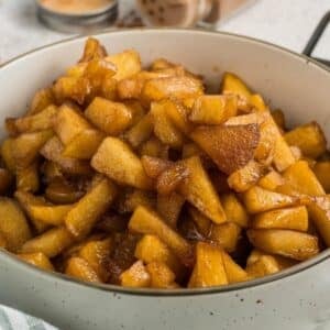 A bowl filled with cooked, diced apples coated in a brown, glossy sauce, likely cinnamon and sugar.