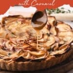 Apple tart topped with thin apple slices on a wooden board, with caramel being drizzled from a spoon.