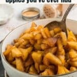 A bowl of fried apple slices with a spoon, topped with cinnamon, set on a table with a small dish of sauce and a spice shaker in the background.