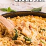 A creamy skillet of sun dried tomato chicken orzo with spinach, stirred by a wooden spoon.
