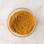 A small glass bowl filled with light brown ground spice, placed on a white speckled surface.
