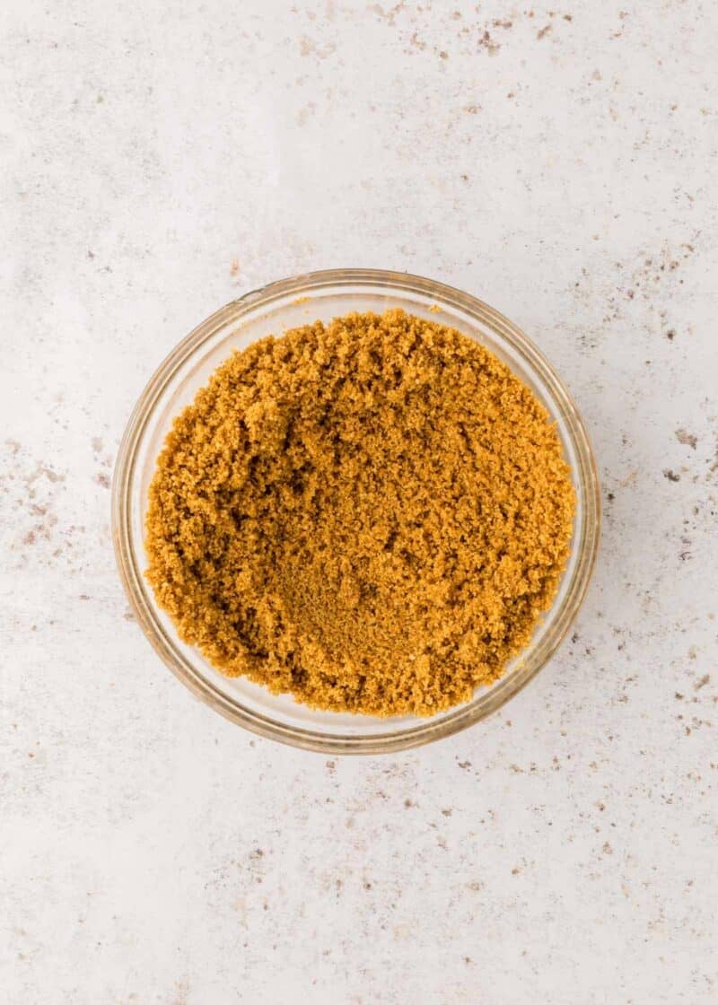 A small glass bowl filled with light brown ground spice, placed on a white speckled surface.