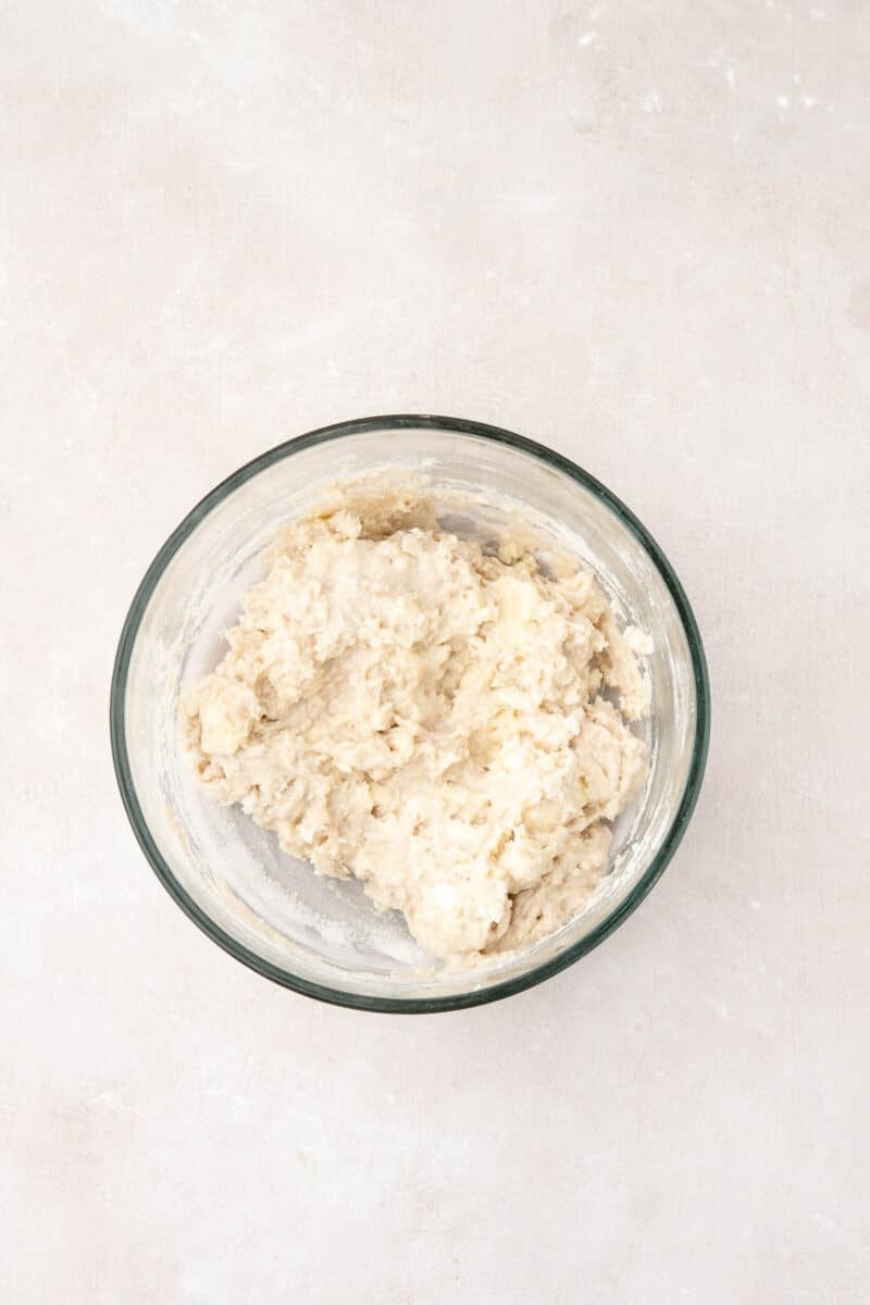 A glass bowl containing mixed dough sits on a light-colored surface.