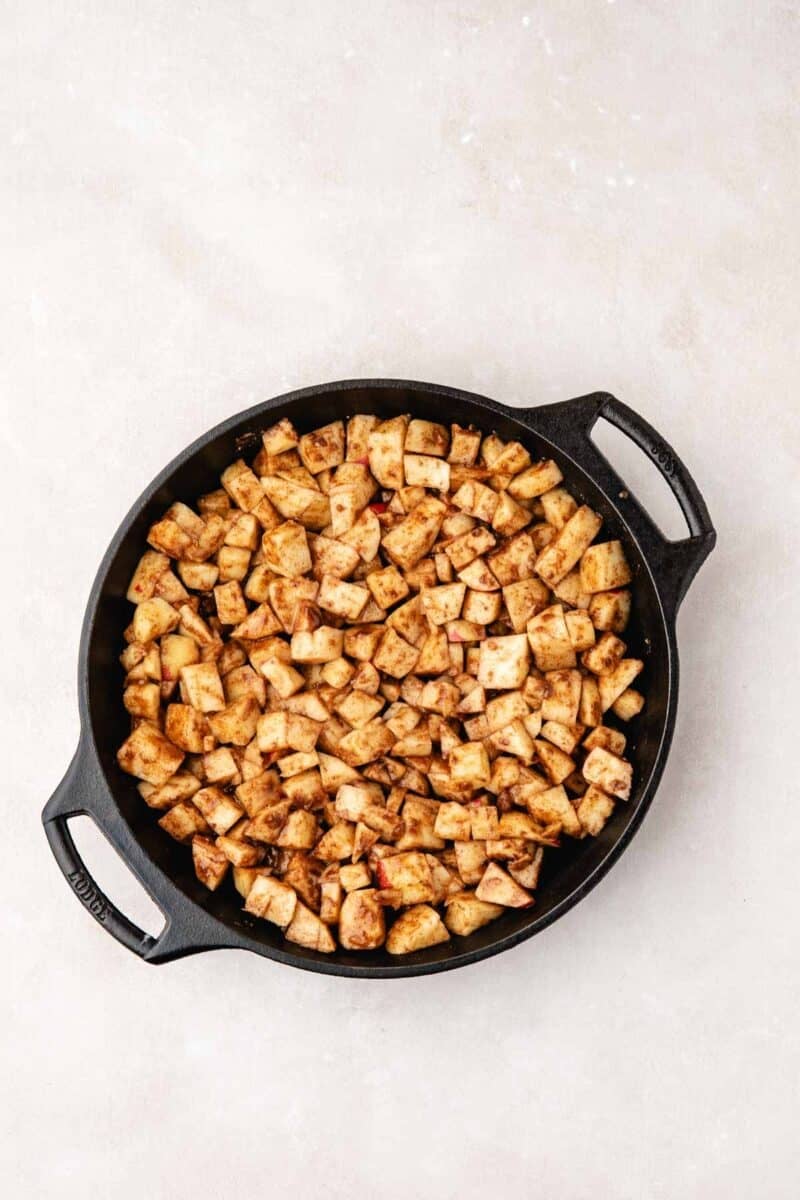 Cubed, seasoned potatoes are spread evenly in a black cast iron skillet on a light-colored surface.