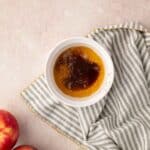 A bowl of melted butter on a striped cloth napkin, with two apples placed nearby on a light-colored surface.