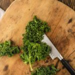 Chopped kale on a wooden cutting board with a knife beside it, set on a rustic wooden surface.