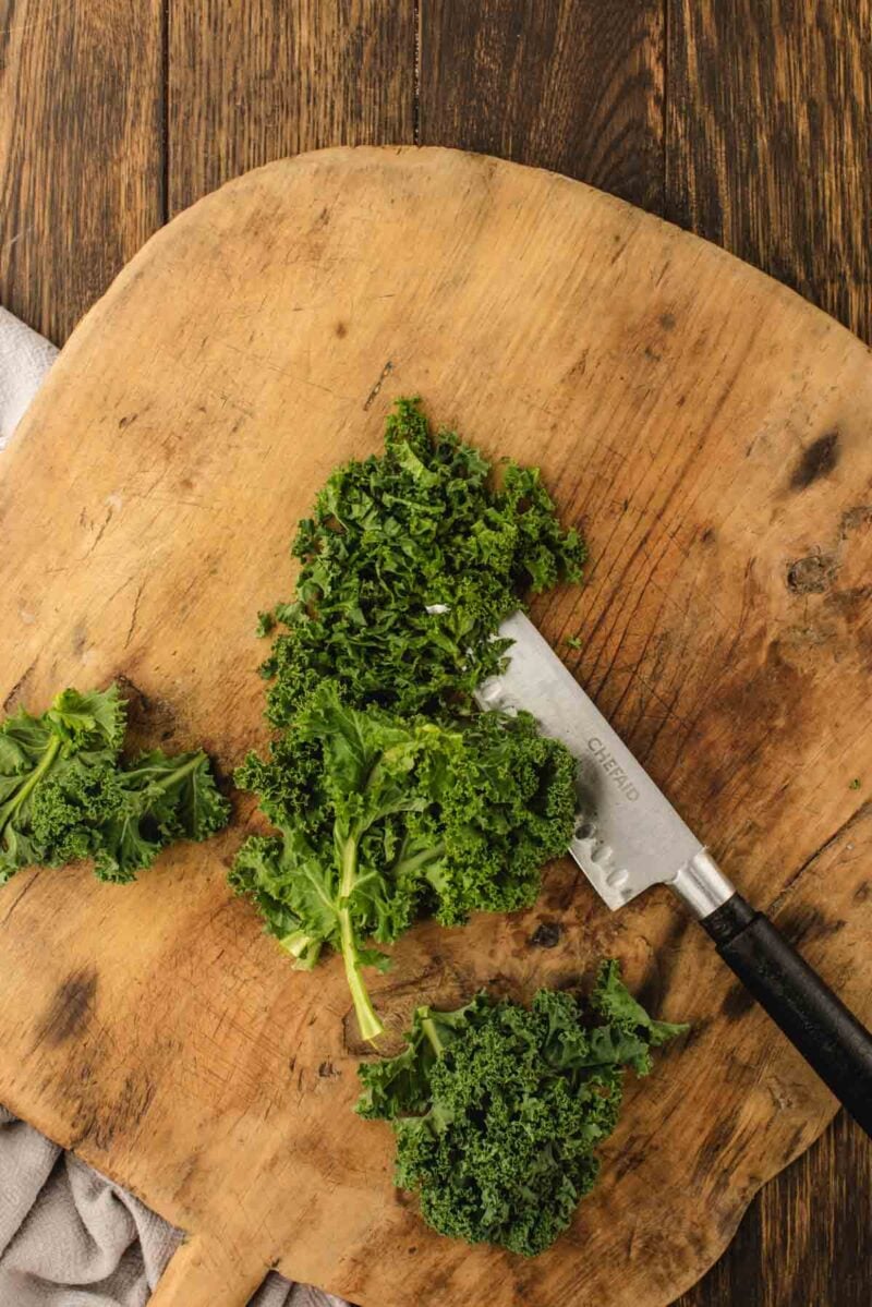 Chopped kale on a wooden cutting board with a knife beside it, set on a rustic wooden surface.