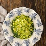 Chopped Brussels sprouts in a white bowl with blue floral designs, placed on a wooden table next to a light-colored cloth.