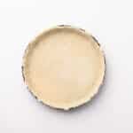 Unbaked pie crust in a round tart pan, viewed from above on a plain white background.