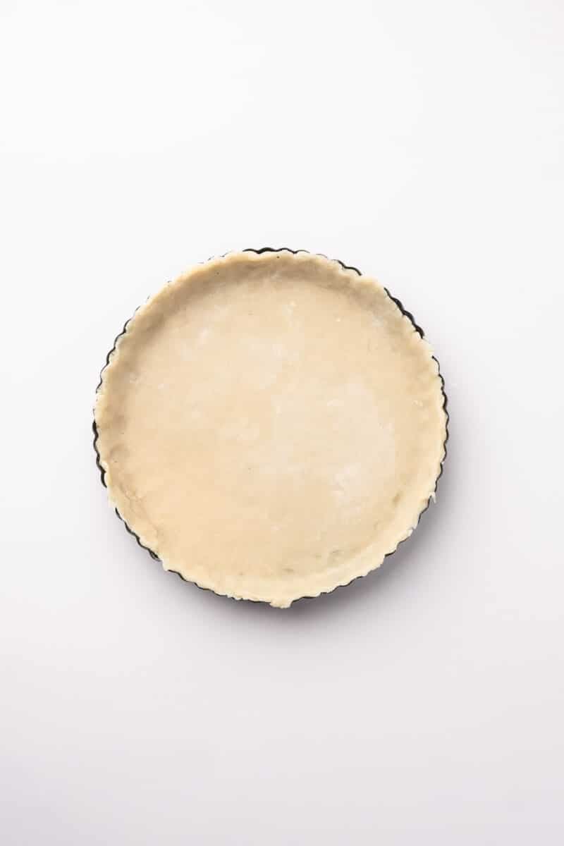 Unbaked pie crust in a round tart pan, viewed from above on a plain white background.