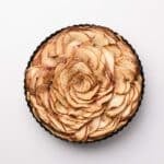 A round tart with thinly sliced apples arranged in a rose pattern, photographed from above on a white background.