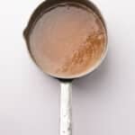 A metal saucepan filled with light brown liquid, viewed from above on a white background.