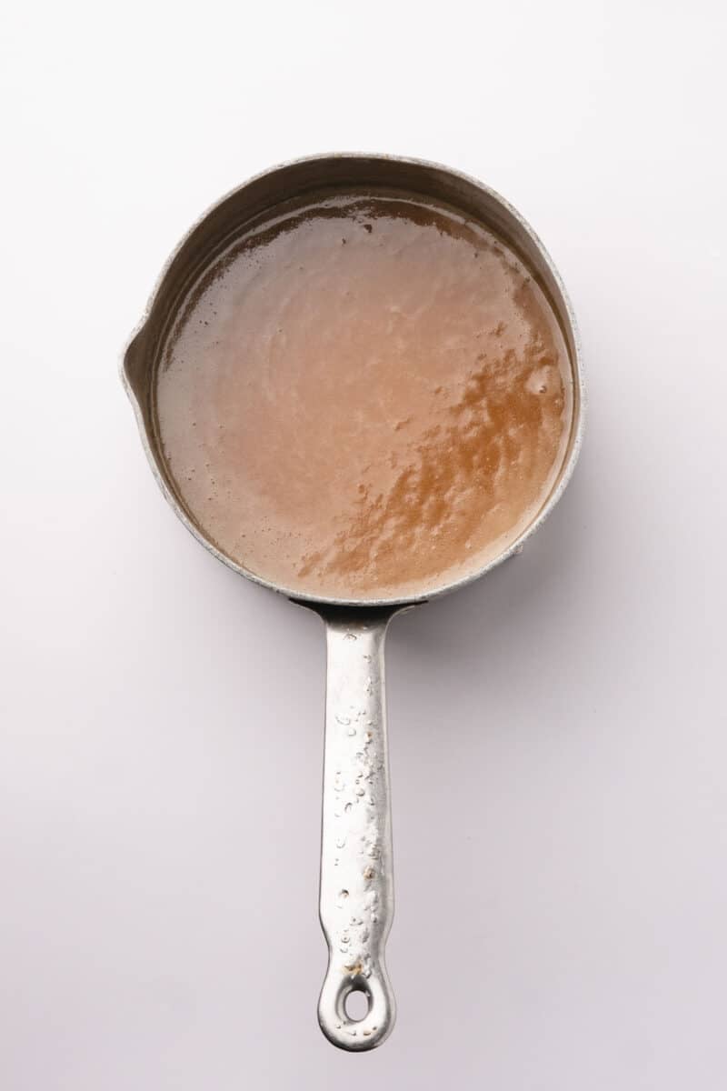 A metal saucepan filled with light brown liquid, viewed from above on a white background.