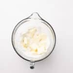 A glass mixing bowl with flour and several pieces of cubed butter on a white surface.