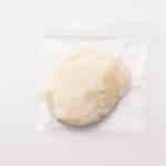 A round portion of dough inside a clear resealable plastic bag on a plain white background.