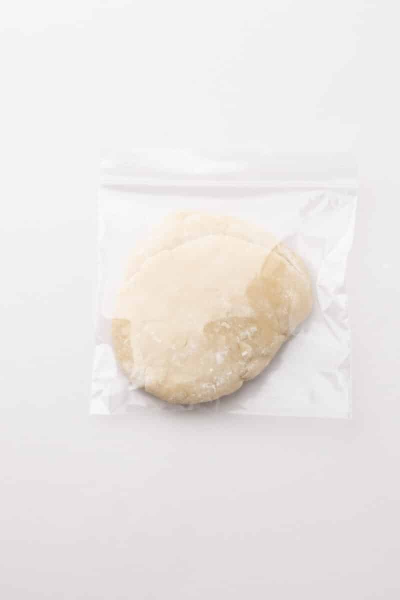 A round portion of dough inside a clear resealable plastic bag on a plain white background.