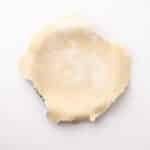 Unbaked rolled-out pie crust placed in a metal pie dish on a white background.