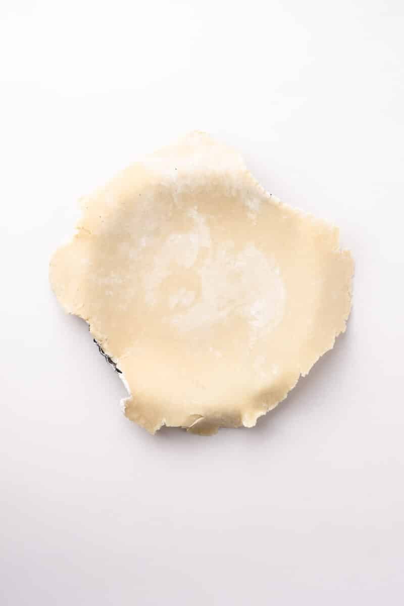 Unbaked rolled-out pie crust placed in a metal pie dish on a white background.
