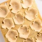A muffin tin filled with unbaked pie dough pressed into each cup, with a pastry brush and small bowl of oil nearby.