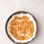 A round springform pan filled with a cream layer, topped with small diced cooked apples, sits on a light surface.