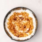 A round pan filled with a cheesecake topped with a swirl of diced caramelized apples and sauce on a light surface.