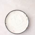 A round cake pan filled with a smooth, white batter sits on a light beige surface, viewed from above.