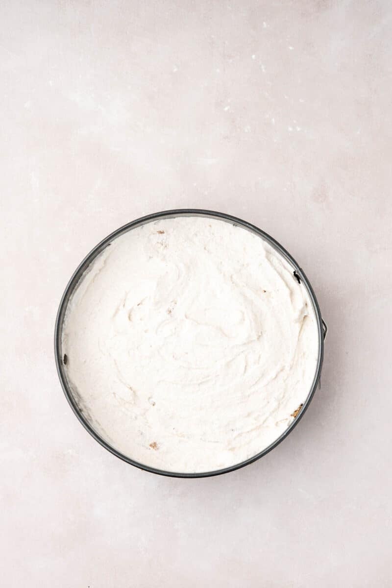 A round cake pan filled with a smooth, white batter sits on a light beige surface, viewed from above.