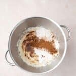 A mixing bowl with brown sugar, powdered sugar, cream cheese, and cinnamon on a light surface, ingredients not yet mixed together.