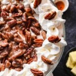A pecan pie trifle topped with whipped cream and whole pecans, with a center layer of pecans in a syrupy sauce, served in a glass dish.
