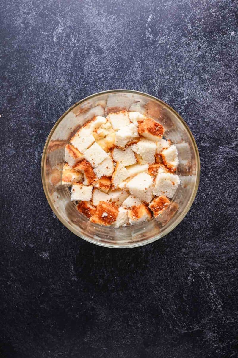 A clear bowl filled with cubed pieces of bread sits on a dark textured surface.