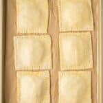 A baking sheet with six unbaked, square hand pies arranged in two columns on parchment paper.