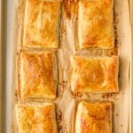 Six golden-brown rectangular pastries are arranged on a parchment-lined baking sheet.