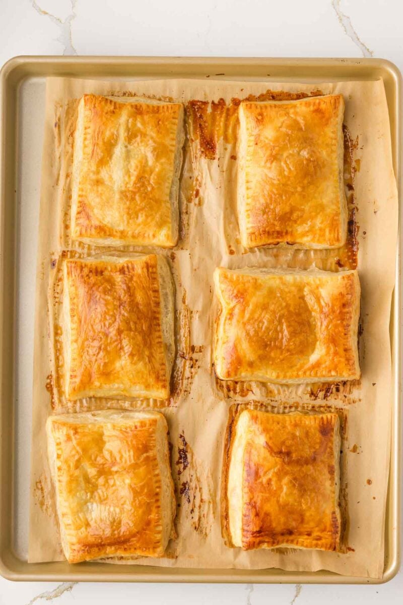 Six golden-brown rectangular pastries are arranged on a parchment-lined baking sheet.
