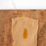 A small amount of honey on a piece of brown parchment paper, placed on a wooden surface with a white background above.