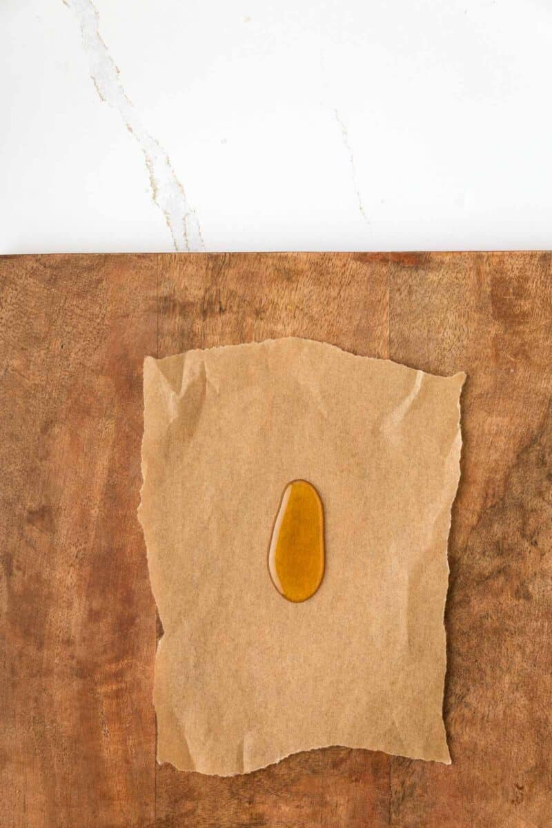 A small amount of honey on a piece of brown parchment paper, placed on a wooden surface with a white background above.