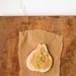 A slice of pear topped with brown sugar sits on a piece of brown parchment paper on a wooden surface, with a white countertop in the background.