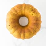 A golden-brown bundt cake is shown from above on a white marble surface.