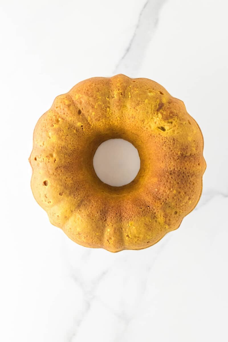 A golden-brown bundt cake is shown from above on a white marble surface.