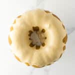 A round bundt cake with white icing drizzled on top, photographed from above on a white marble surface.