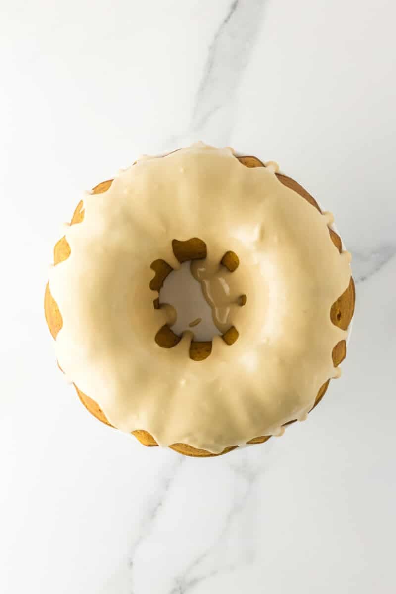 A round bundt cake with white icing drizzled on top, photographed from above on a white marble surface.