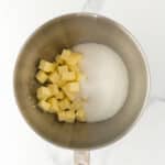 A metal mixing bowl containing cubed butter and granulated sugar on a white marble surface.