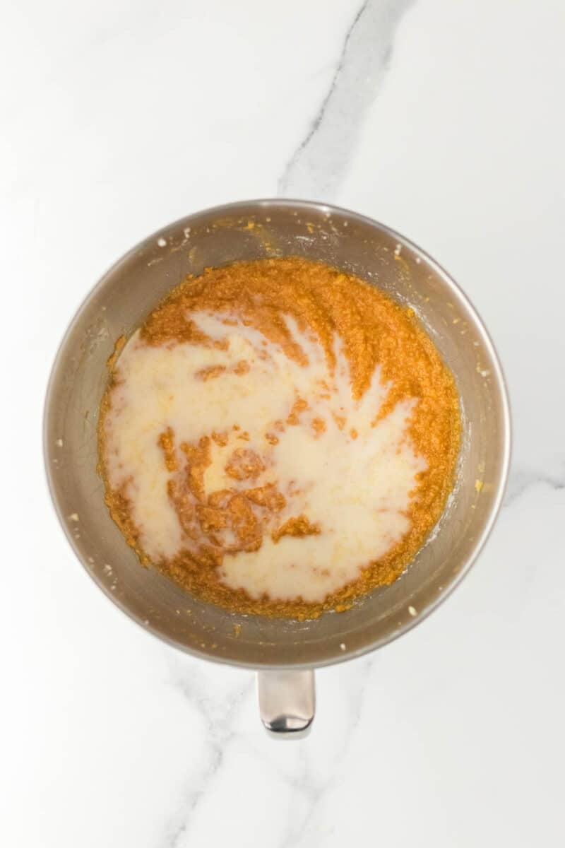 A metal mixing bowl containing a mixture of brown batter and white liquid, sitting on a white marble surface.