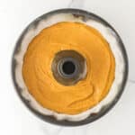 A bundt pan filled with unbaked orange cake batter sits on a white marble surface.