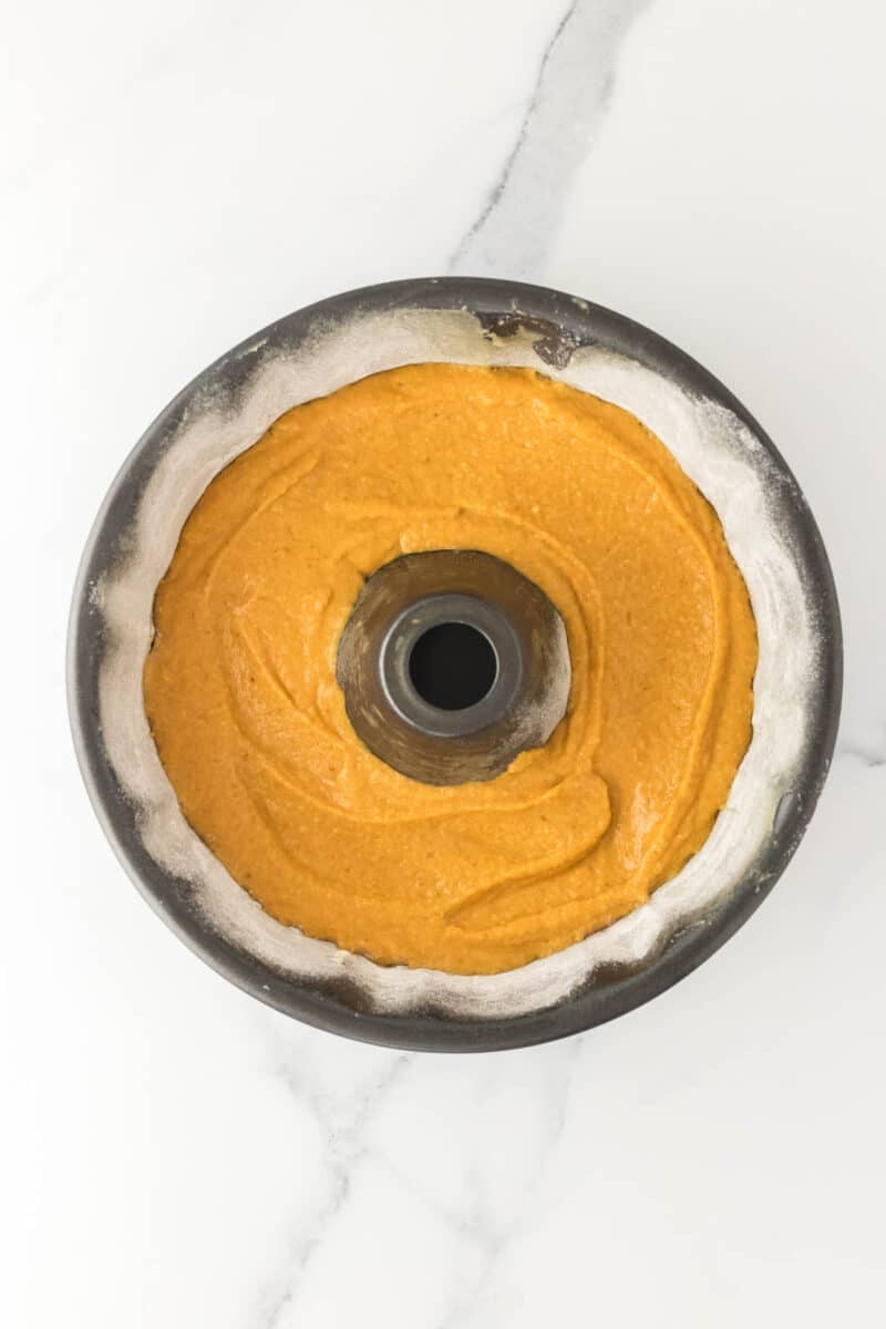 A bundt pan filled with unbaked orange cake batter sits on a white marble surface.