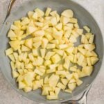 Overhead view of chopped apples in a large skillet on a light surface.