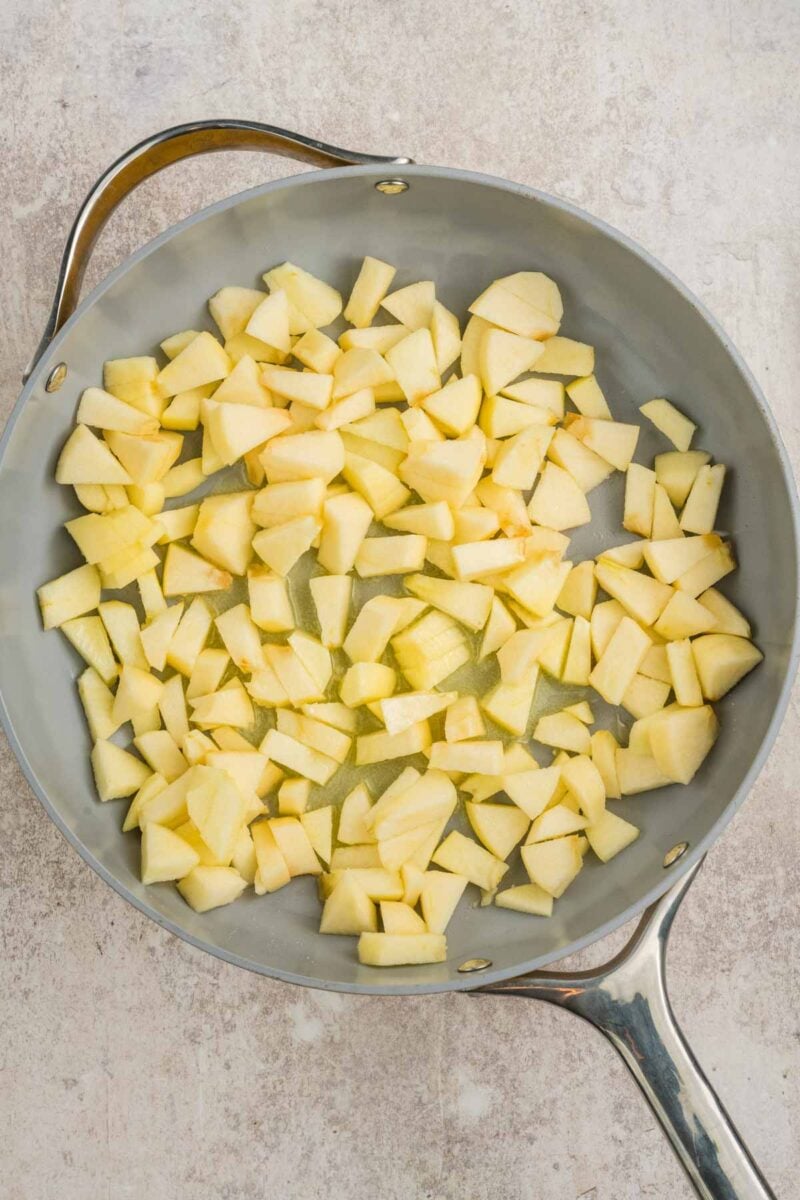 Overhead view of chopped apples in a large skillet on a light surface.
